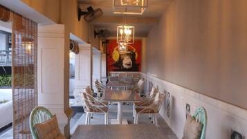 A narrow corridor with a dining area featuring a long table and chairs, a hanging light fixture, and a mural on the wall.