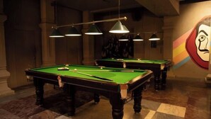 A pool table with a green felt surface, surrounded by dark wooden legs and a checkered floor. - Hotel FORT28 (Nagpur)