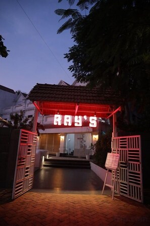 A building entrance with a neon sign, a gated pathway, and a small outdoor seating area. - Hotel FORT28 (Nagpur)