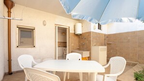 A patio area with a white table and chairs, a blue umbrella, a shower, and a kitchen visible through an open door. - Apartment 'Corte Nonna Mmela' with Private Terrace, Wi-Fi and Air Conditioning (melendugno)