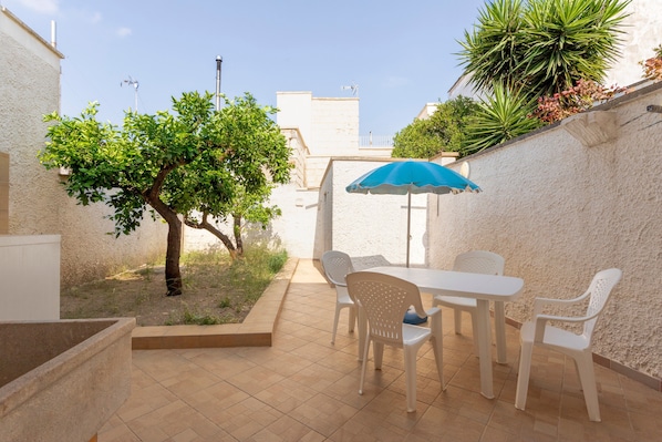 A patio with a table and chairs, a blue umbrella, and a tree.