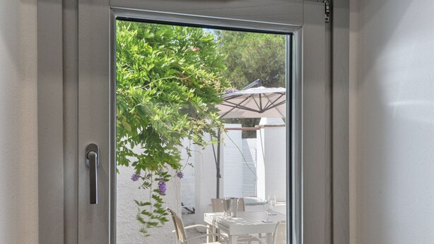 Une porte donnant sur un patio extérieur, avec une table, des chaises et un arbre aux fleurs violettes.