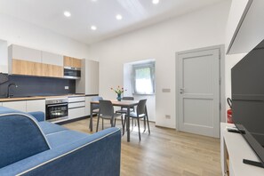 A modern kitchen with a dining area, a sofa, and a door with a fire extinguisher.