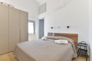 A bedroom with a bed, a wardrobe, a small table, and a window.