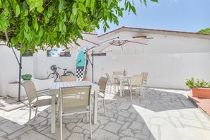 An outdoor patio area with a table and chairs, a bicycle, and a surfboard leaning against a wall.