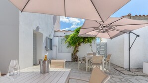 Un espace patio aménagé avec une table, des chaises, un verre à vin, une bouteille et des parasols.