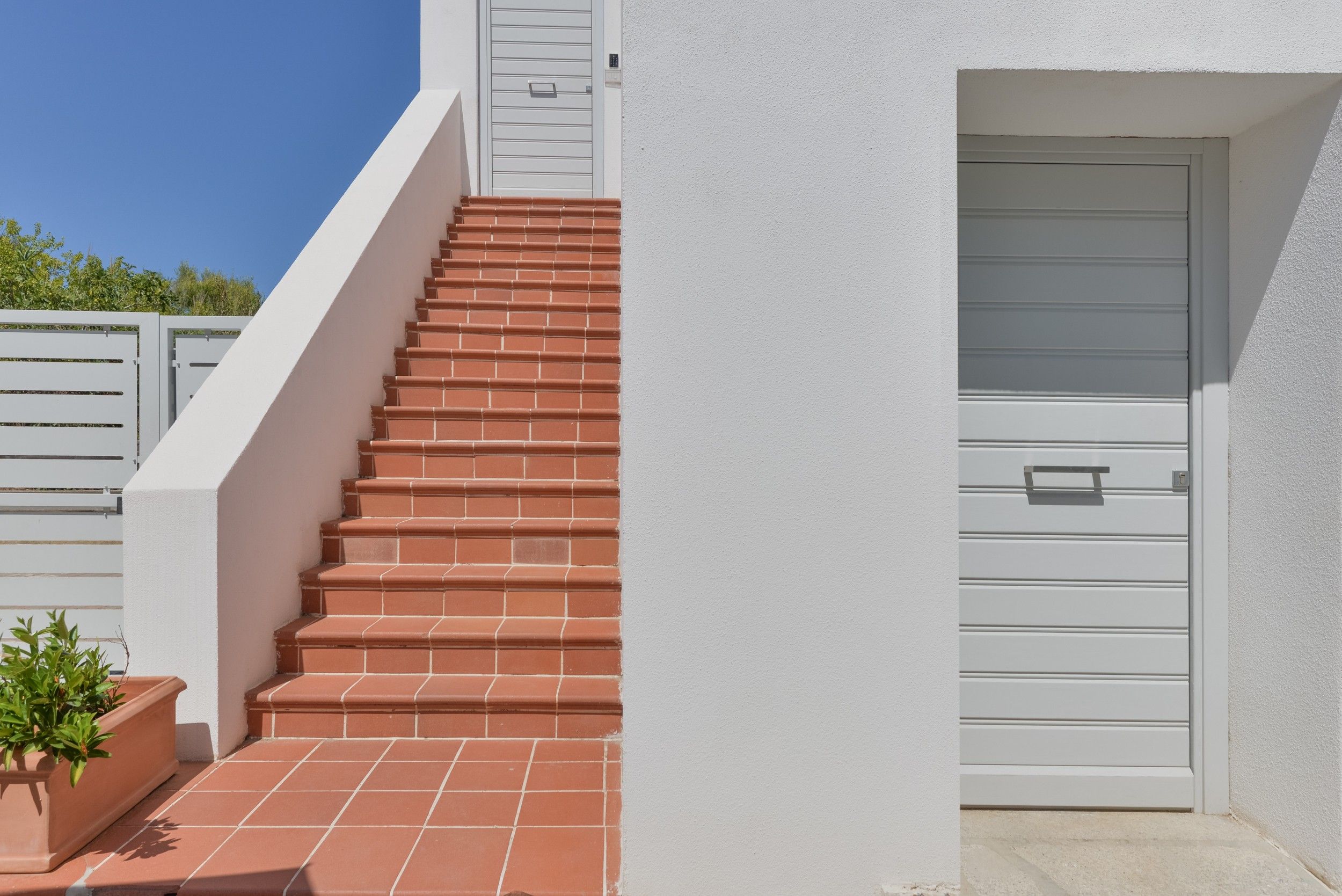 Unos escalones rojos con tejas que conducen a una puerta blanca con paneles horizontales.