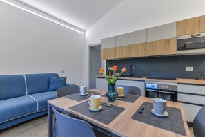 Moderni keittiö, jossa on sisäänrakennettu uuni ja mikroaaltouuni, ruokapöytä, jossa on aluslautasliinat, ja sininen sohva.