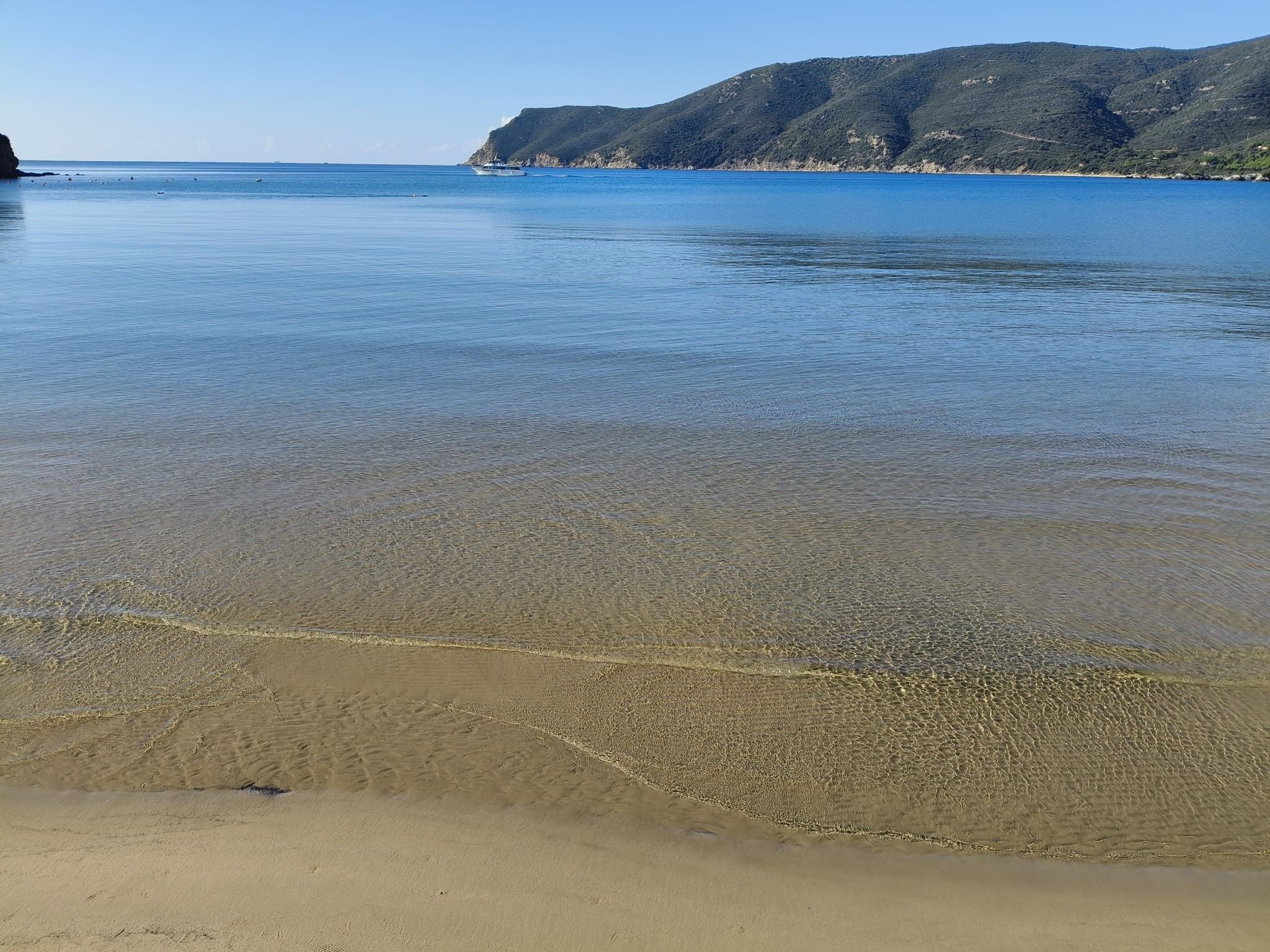A beach with clear shallow waters, a sandy shore, and a distant mountain range.
