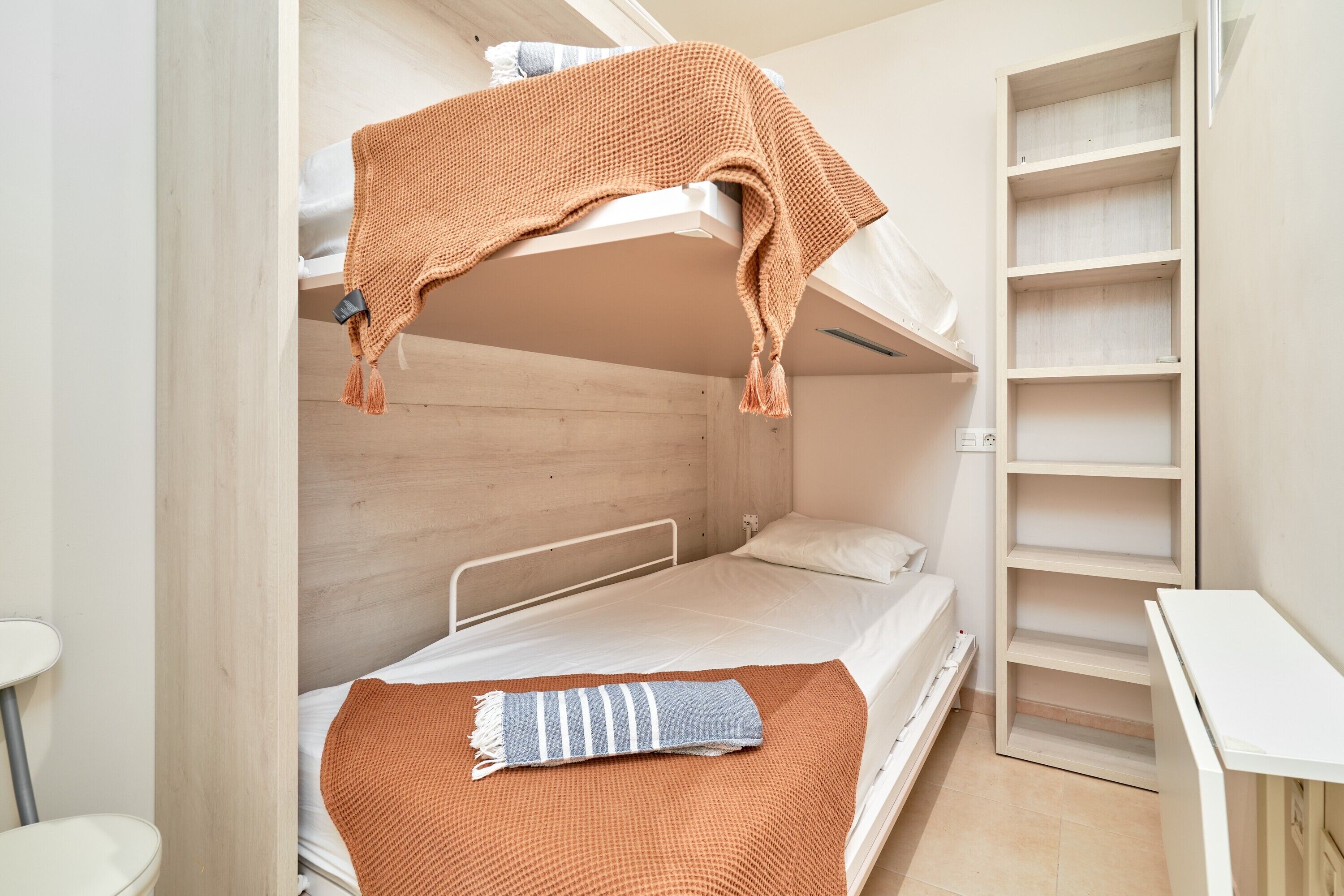 A bunk bed with a blanket, a small desk, and a shelving unit.