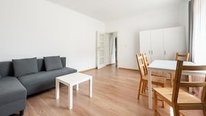 A modern living room with a grey sofa, a white coffee table, wooden chairs, and a white dining table. - Nowolipki Standard Studio (Warszawa)