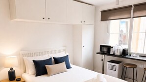 Habitación de hotel con cama, mesita de noche, lámpara, toallas enrolladas, escritorio con microondas, tostadora y una silla.