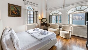 A hotel room with a bed, two armchairs, a mirror, and a view of the sea. - Lake Front Villa Schlosser (Malcesine)