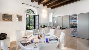 A dining area with a round table set for four, white chairs, a window with a view of greenery, and a kitchen area with cabinets and a microwave. - Lake Front Villa Schlosser (Malcesine)