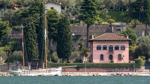 A coastal building with a red-tiled roof, a balcony, and a stone wall. - Lake Front Villa Schlosser (Malcesine)