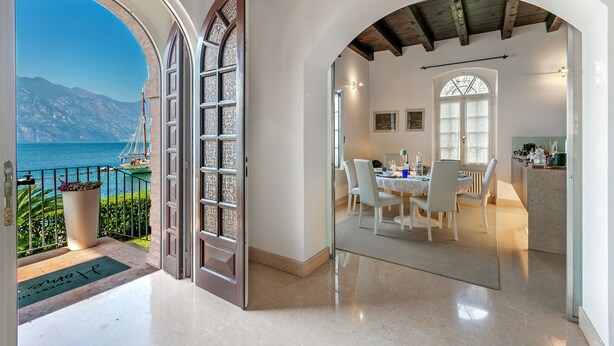 A modern hotel interior with a dining area, kitchen, and a balcony with a view of the sea and mountains. - Lake Front Villa Schlosser (Malcesine)