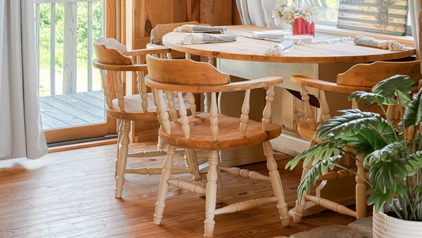 A wooden cabin interior with a dining table, chairs, and a view of greenery outside. - The Rustic Retreat: Elegant cabin with WiFi & AC in an enchanting location! (Pearl City)