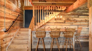 A wooden staircase leading to a bar area with three wooden chairs. - The Rustic Retreat: Elegant cabin with WiFi & AC in an enchanting location! (Pearl City)