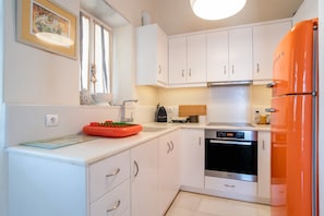 A kitchen with white cabinets, a black oven, and an orange refrigerator.