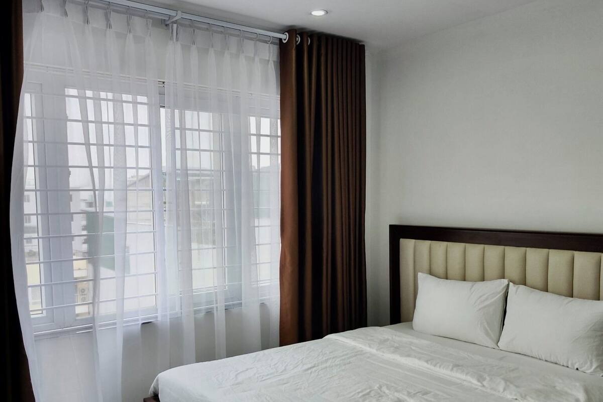 Una habitación de hotel moderna con una cama grande, cabecera y ventana con cortinas traslúcidas.