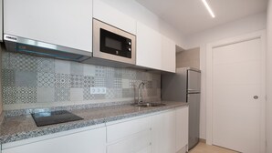 Une cuisine avec des meubles blancs, un four à micro-ondes en acier inoxydable, un réfrigérateur et un crédence décorée.