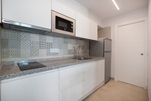 Et køkken med hvide skabe, en rustfri mikroovn, et køleskab og et mønstret backsplash.