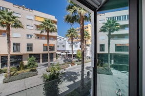 A modern building with multiple floors, palm trees, and a paved outdoor area with seating.