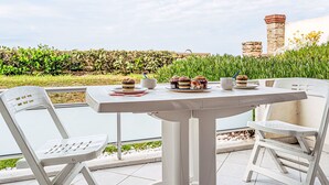 An outdoor patio with a white table and chairs, a view of a garden, and a stone wall in the background. - Penduick by Interhome (Quiberon)