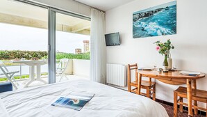 A hotel room with a bed, a small table with chairs, a TV on the wall, and a balcony with a table and chairs. - Penduick by Interhome (Quiberon)
