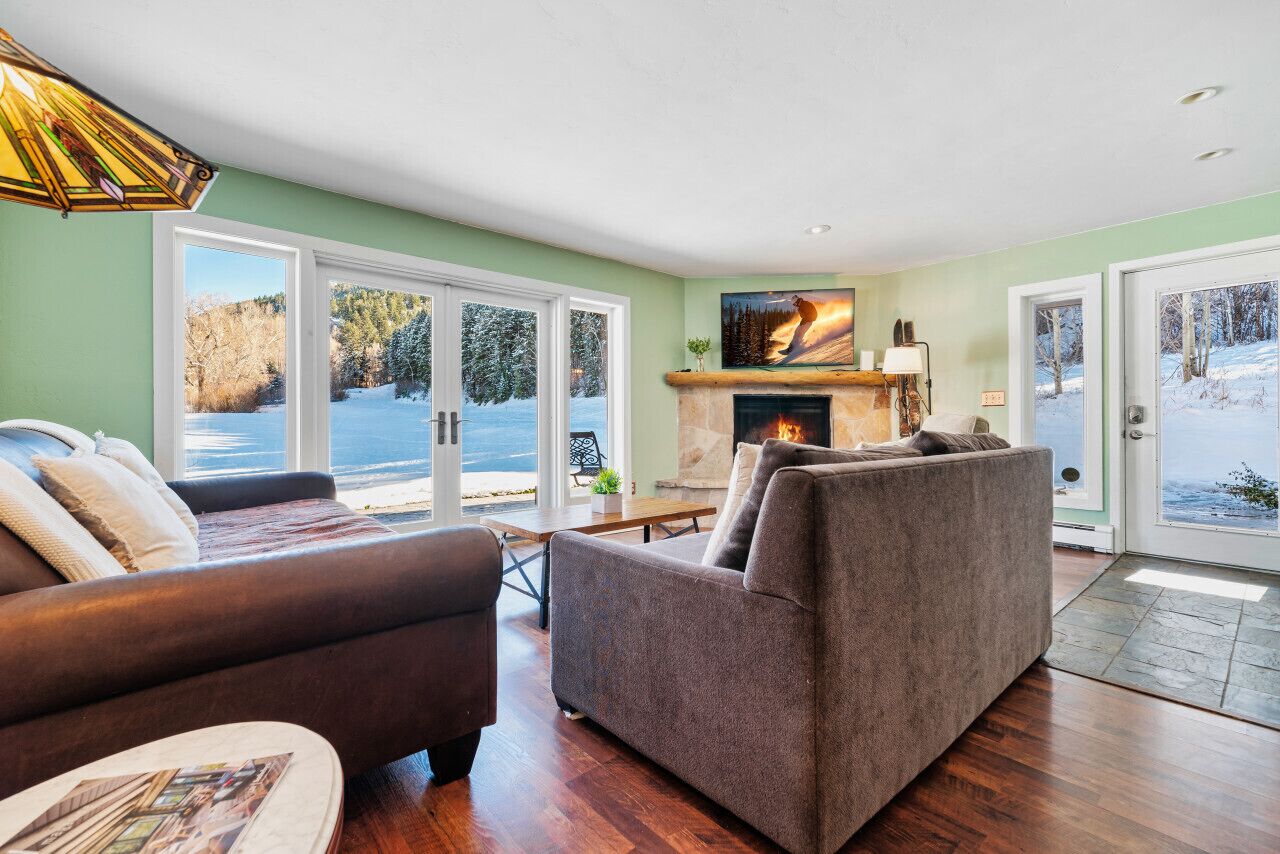 A cozy living room with a fireplace, large windows, and a view of a snowy landscape.