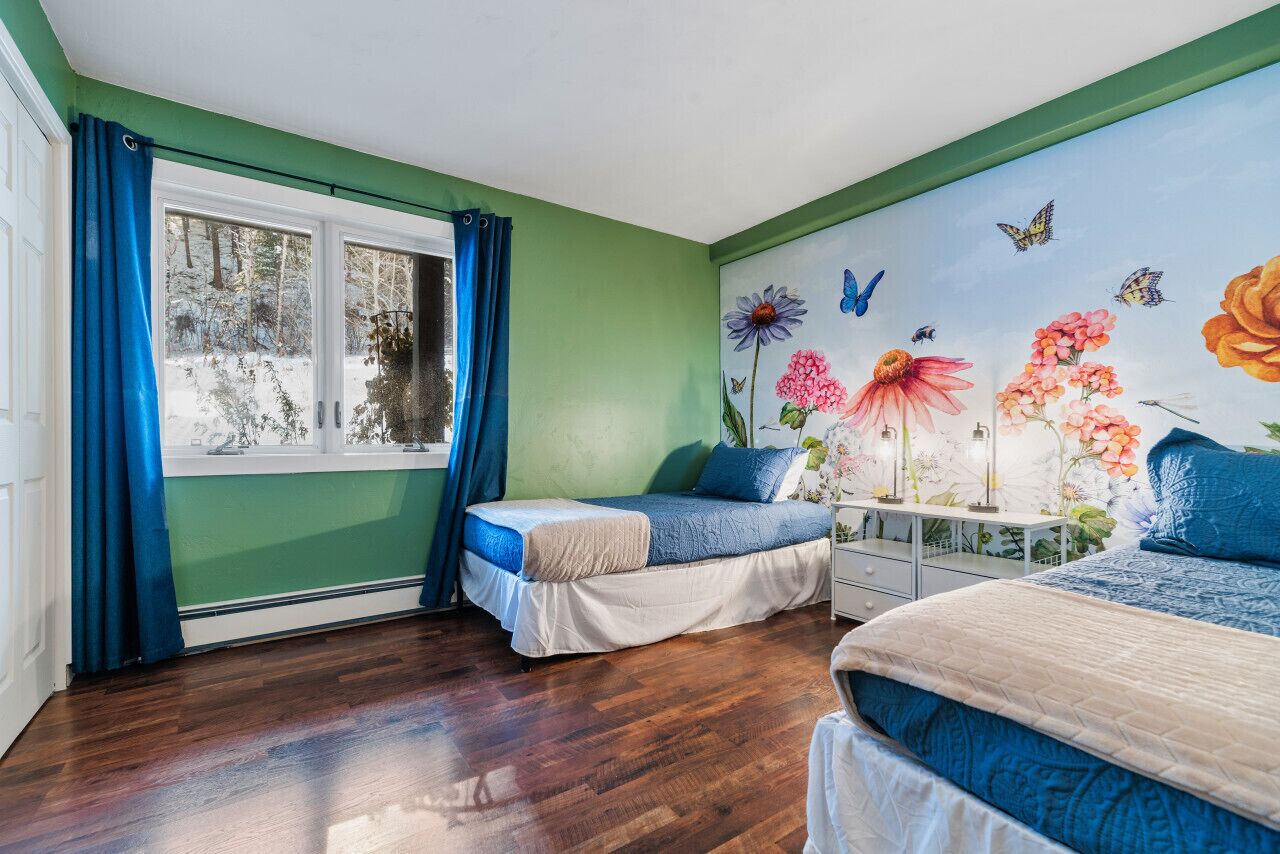 Una camera da letto con due letti, una finestra con tende blu e un murale floreale con farfalle.