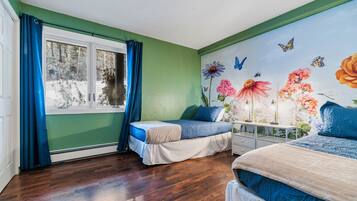 Una camera da letto con due letti, una finestra con tende blu e un murale floreale con farfalle.
