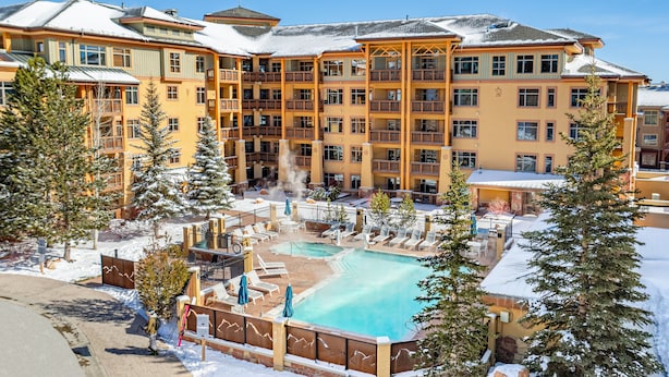 A multi-story hotel with a pool area, outdoor seating, and snow-covered surroundings. - Sundial condo in Canyons Village, private patio, outdoor pool & hot tub, walk to hiking and biking (Park City)