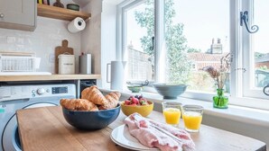 A kitchen with a wooden table, a bowl of croissants, a plate of raw chicken, a bowl of berries, and glasses of orange juice.