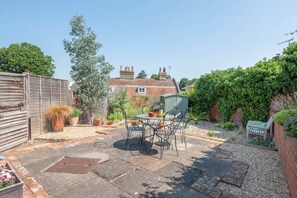 Ein Patio mit Tisch und Stühlen, umgeben von Kübelpflanzen und einer kleinen Gartenhütte.