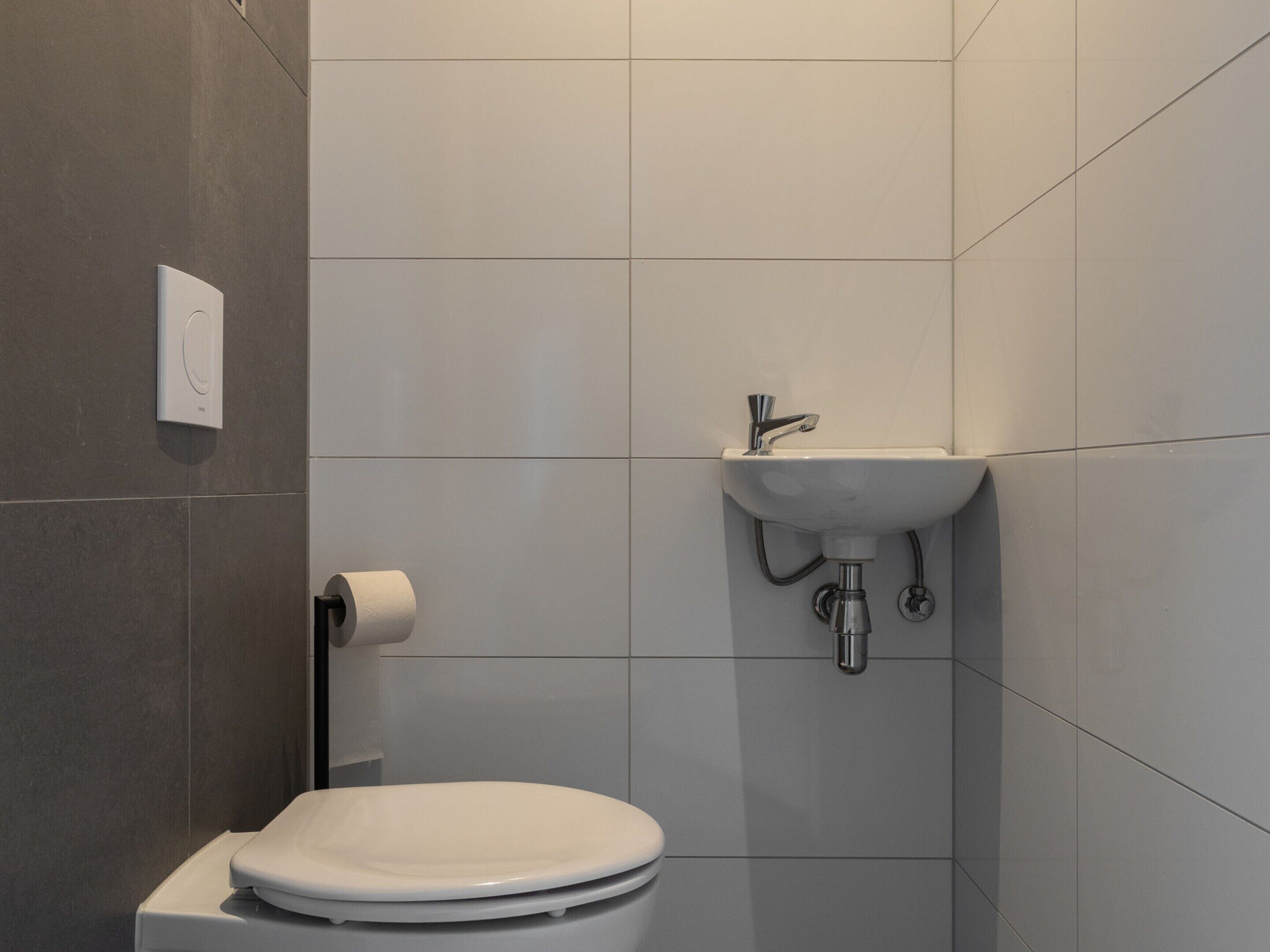 Un baño moderno con inodoro, lavamanos y dispensador de papel higiénico.