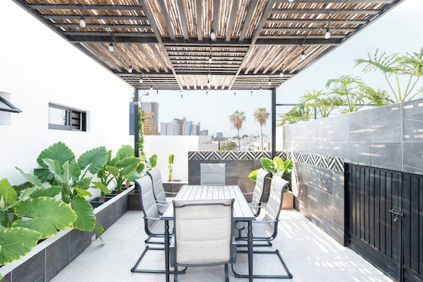 A patio with a table and chairs, surrounded by plants and a view of the cityscape.