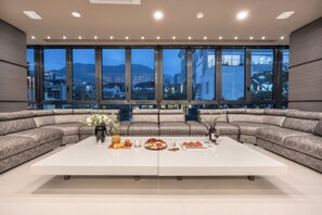 A modern living room with a large sectional sofa, a white coffee table, and a city view through large windows. - Luxury 4BR Glass Penthouse right in Lleras Park (Medellin)