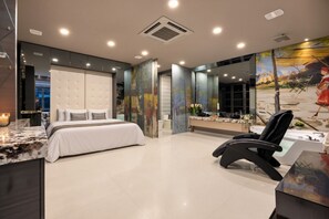 Une chambre d’hôtel moderne dotée d’un grand lit, d’un coin salon avec un fauteuil, d’un bureau et d’une grande fenêtre offrant une vue dégagée.