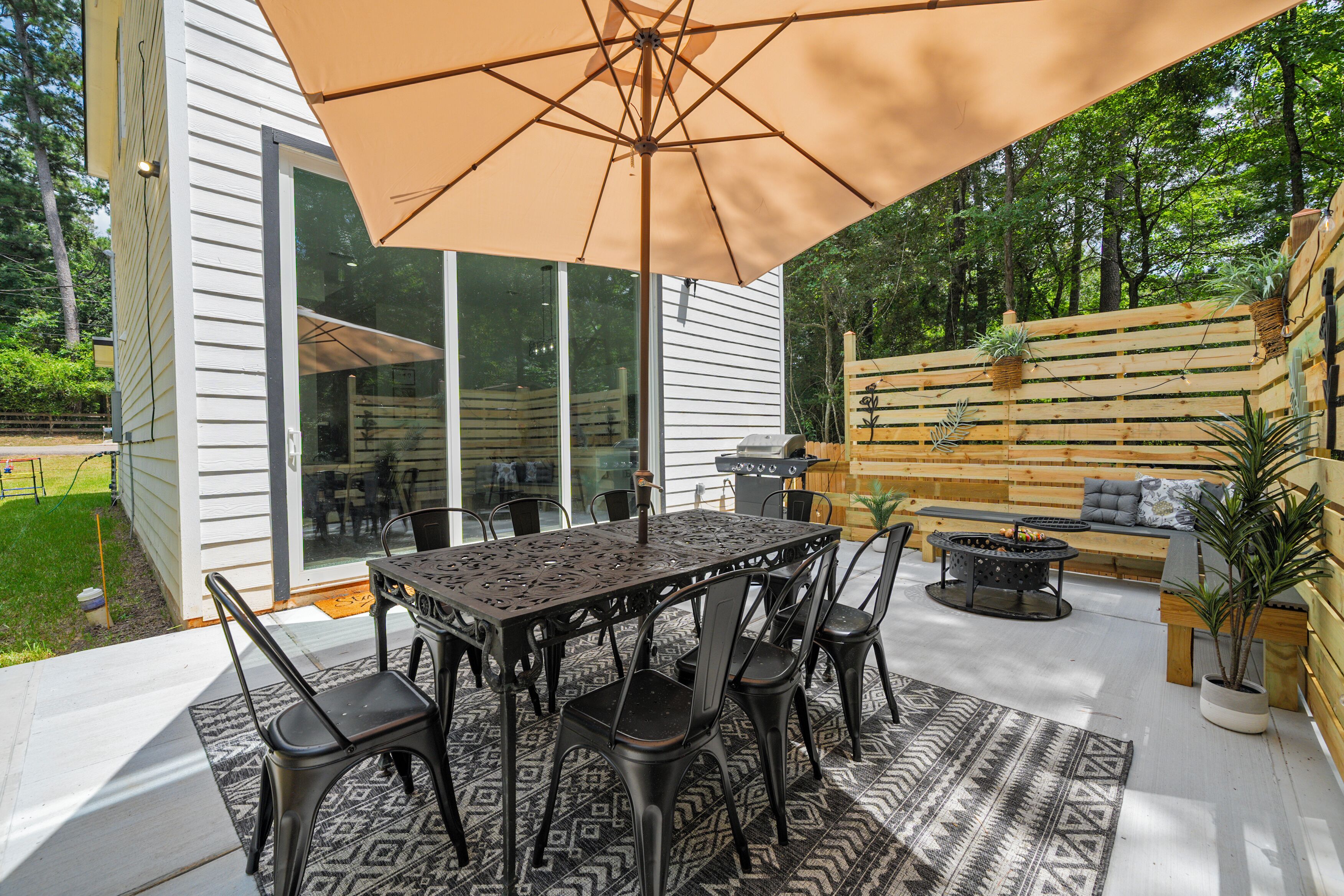 An outdoor patio with a table and chairs, a large umbrella, and a fire pit.