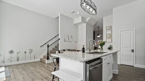 Una cocina moderna con una isla central, electrodomésticos de acero inoxidable y una escalera que lleva a un nivel superior.