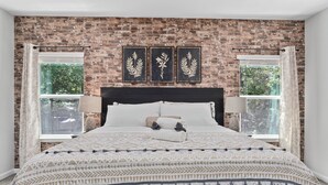 Un dormitorio con pared de ladrillo, cama con ropa de cama estampada y tres obras de arte enmarcadas.