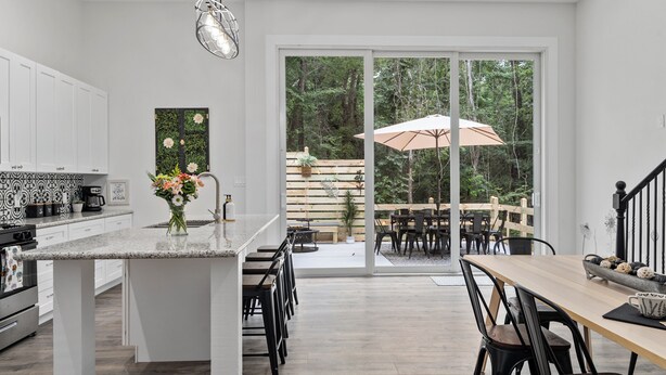 Una cocina moderna con una isla central, muebles blancos y un comedor con mesa y sillas de madera.