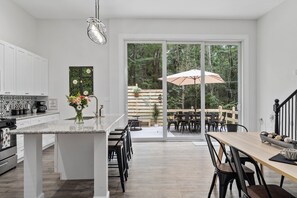Ett modernt kök med en central köksö, vita köksskåp och en matplats med ett träbord och stolar.