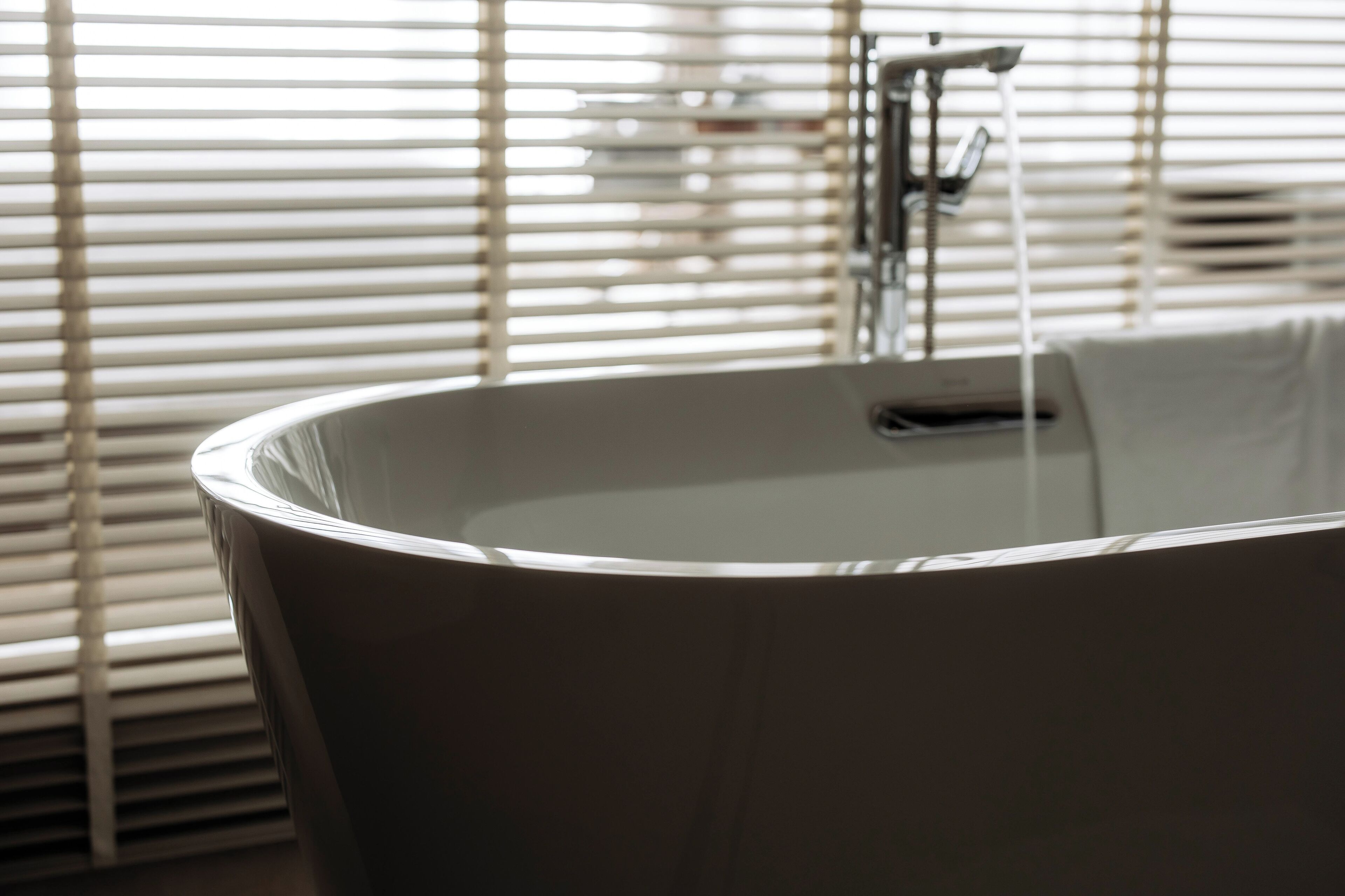 A bathtub with a faucet and a window with blinds in the background.