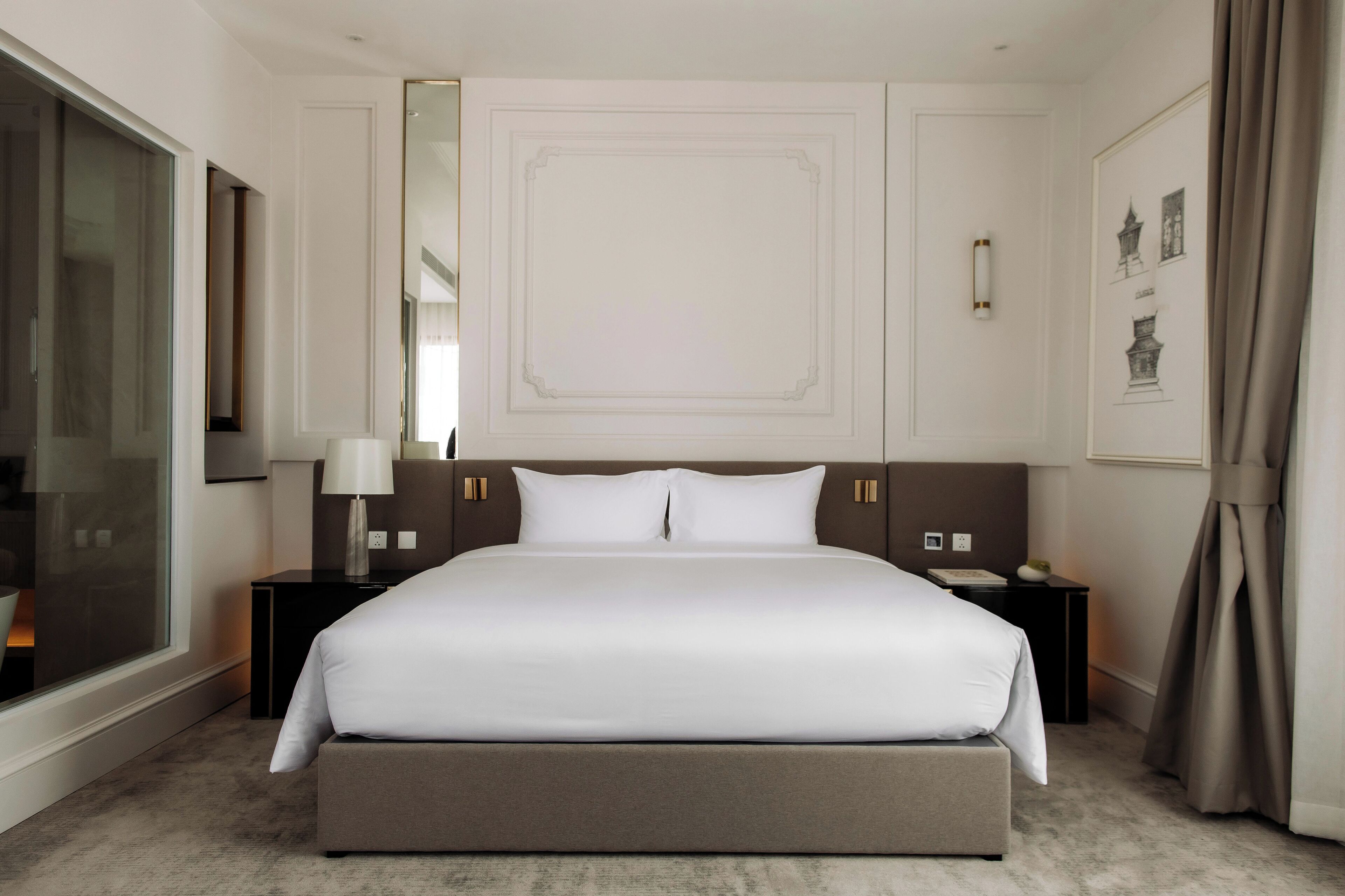 A modern hotel room with a large bed, bedside tables, a mirror, and a window with curtains.