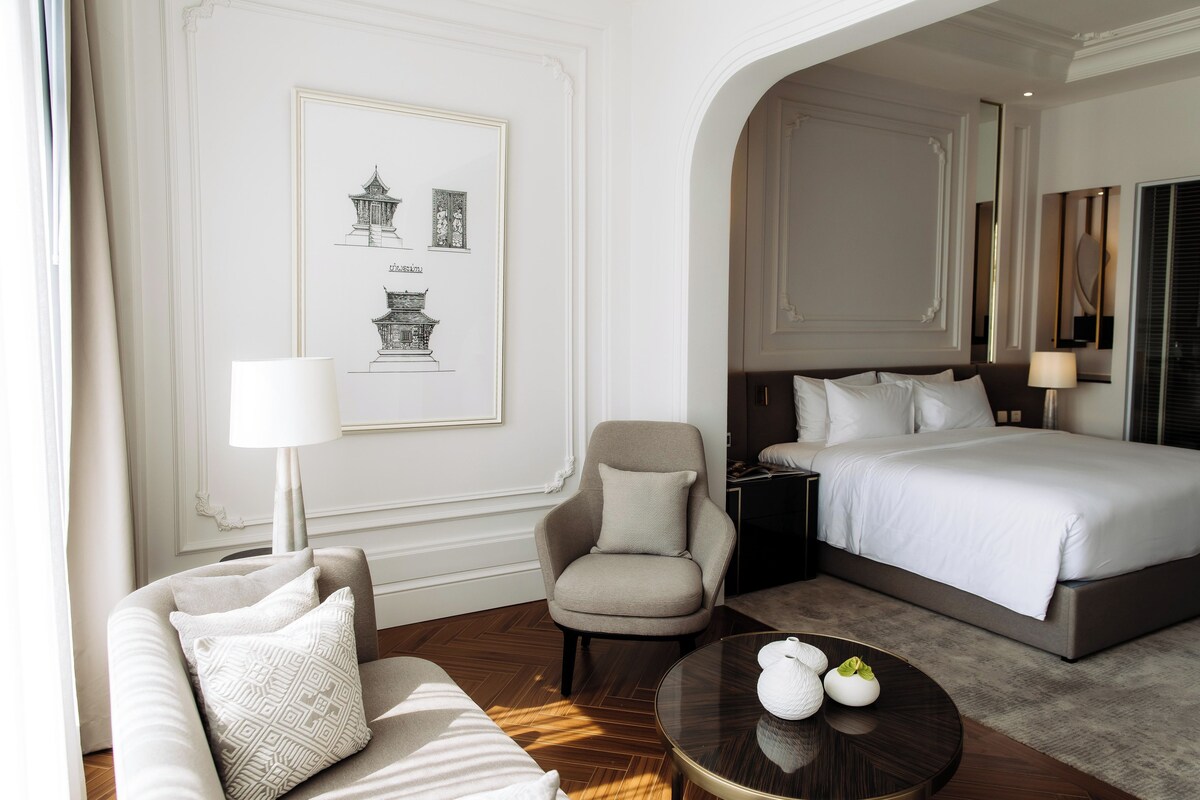 Een hotelkamer met een bed, een stoel, een bank, een ronde tafel en een muur met kunstwerken.
