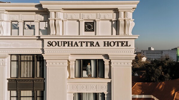 L’extérieur de l’hôtel Souphattra présente un style architectural classique, avec une enseigne bien visible portant le nom de l’hôtel, de grandes fenêtres et une horloge au-dessus de l’entrée.