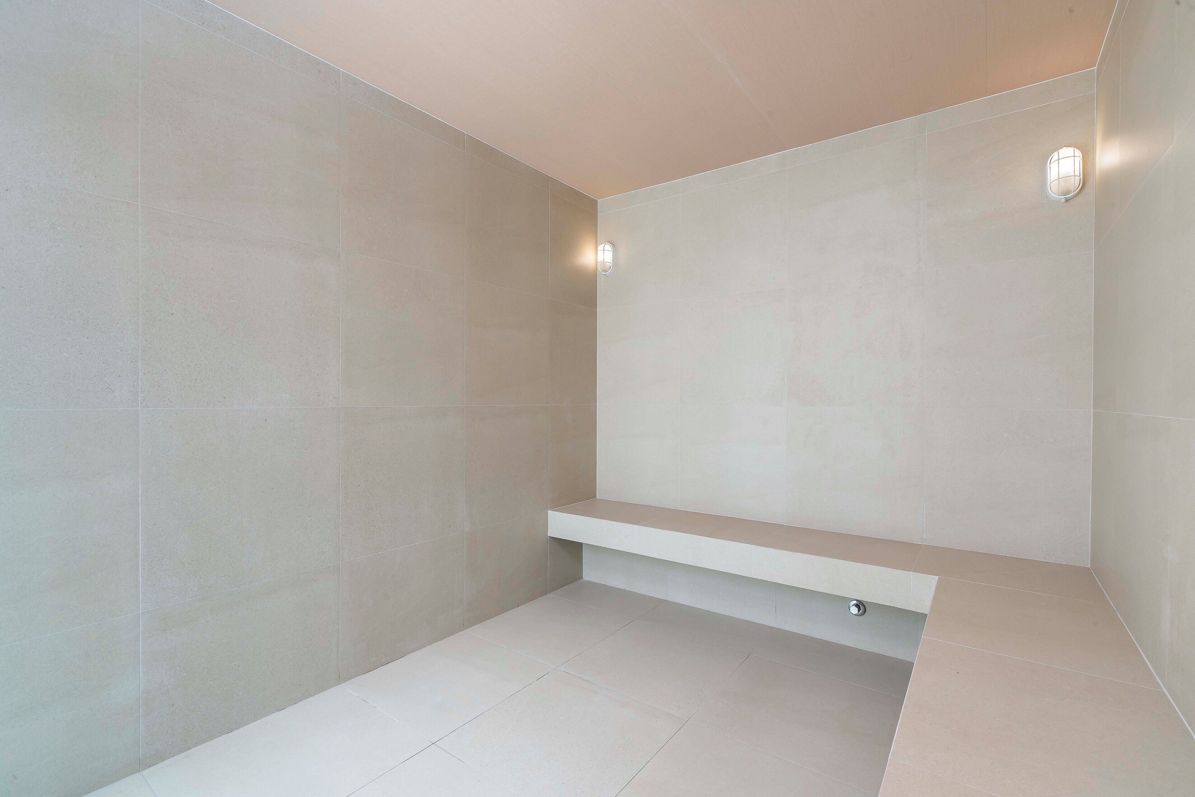 Een moderne badkamer met grote betegelde wanden, een inbouwbank en wandlampen.
