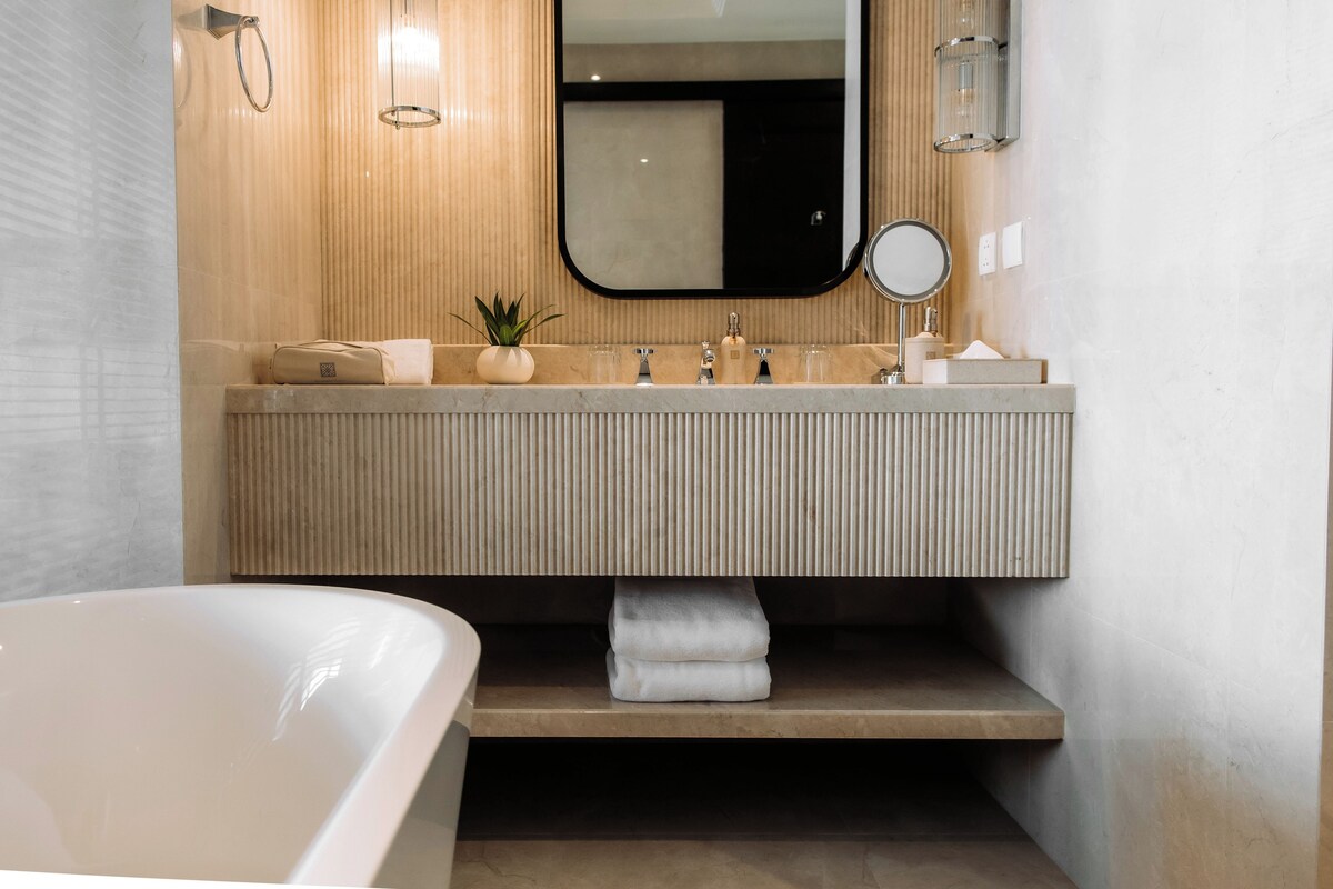 Een moderne badkamer met een groot bad, een houten wastafelmeubel met spiegel en een handdoekrek.